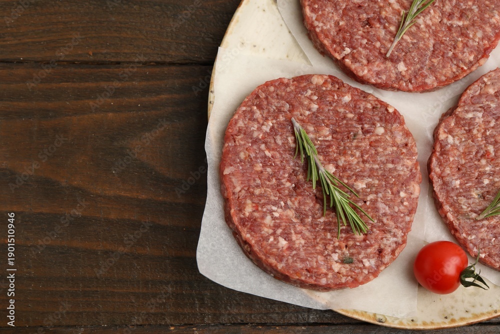 Fototapeta premium Uncooked meat patty with rosemary and tomato on wooden table, flat lay. Space for text