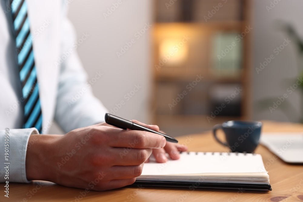 Fototapeta premium Man writing in notebook with pen at wooden desk, closeup