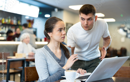 Tablou pe pânză Girl asks her boyfriend not to disturb her while he works on his laptop in a caf