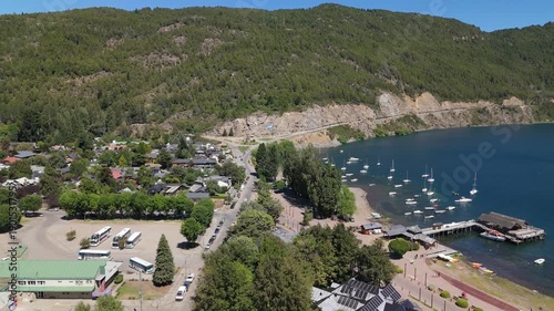 Aerial view of Lake Lacar and San Martin de los Andes in Patagonia, highlighting a scenic marina with numerous sailboats and boats anchored in deep blue water surrounded by mountains.