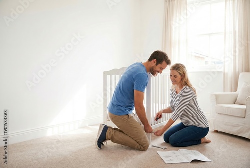 A happy couple works together, smiling, to assemble a new white baby crib in a bright, empty nursery room, preparing for their baby's arrival.