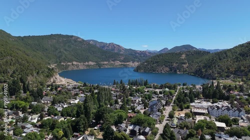 Aerial view of Lake Lacar and San Martin de los Andes in Patagonia, highlighting a scenic marina with numerous sailboats and boats anchored in deep blue water surrounded by mountains.