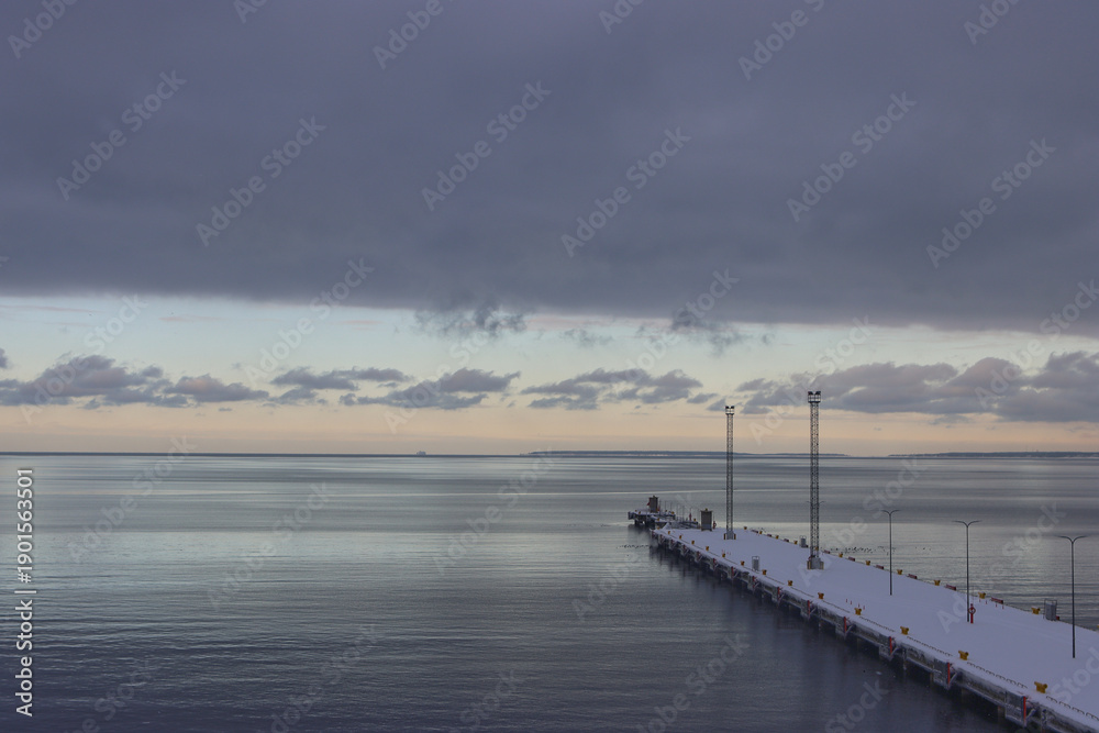 Obraz premium Pier extending into calm sea under dramatic clouds