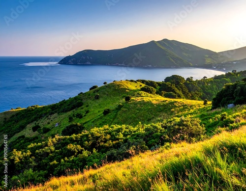 A vibrant coastal scene presents lush green hills meeting the calm blue sea under a golden sunset sky. A scenic landscape