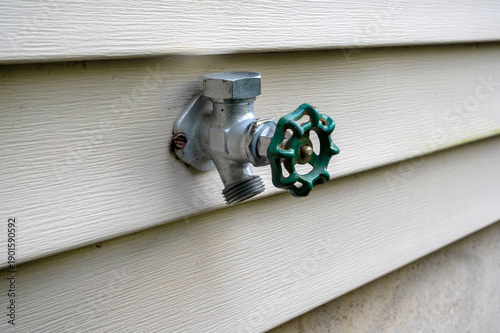 Outdoor water faucet mounted on house exterior wall. House water tap outside