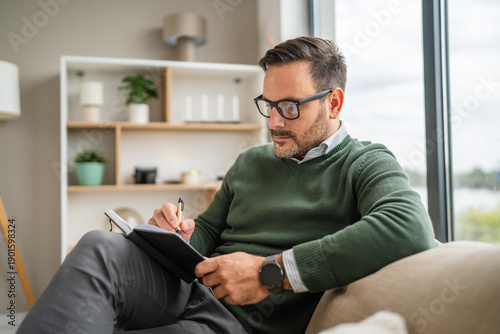 Fotografi Man wearing eyeglasses reading notebook by window relaxation