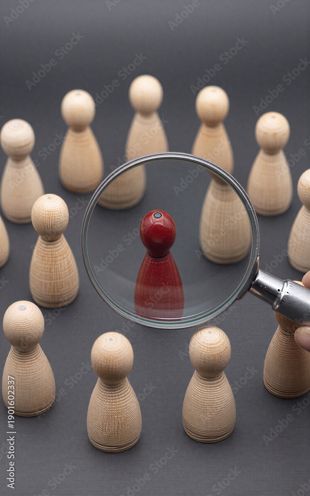 Obraz premium Magnifying glass highlights one red pegman among many beige ones, symbolizing focus or selection.