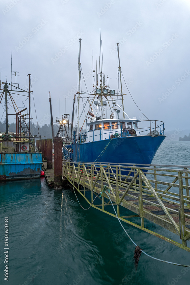 Fototapeta premium The lights are on in the wheelhouse of a commercial fishing trawler docked at dusk near Coos Bay, Oregon, USA
