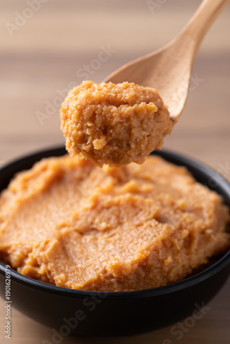 Scooping traditional Japanese miso paste from a black bowl with a wooden spoon, fermented soybean seasoning for cooking