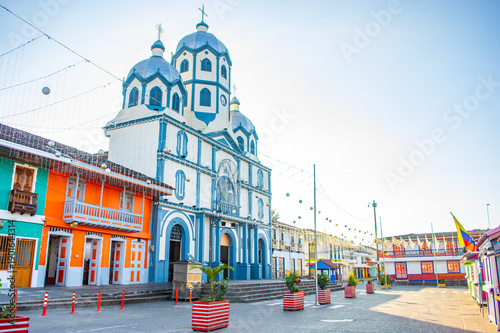 A bright blue church stands out against colorful buildings in Filandia, showcasing vibrant architecture and clear skies.