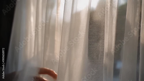 Sunlight filtering through sheer white curtains, casting soft shadows and illuminating dust particles in a peaceful morning scene