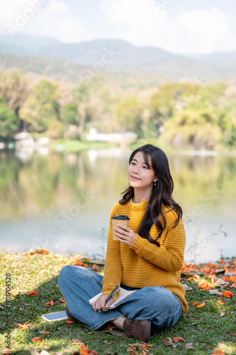 Foto Pretty asian woman holding drinking coffee while sitting crossed legs on grass l