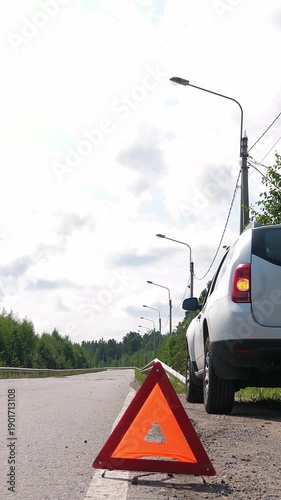Car and red triangle emergency stop sign on asphalt road. Nobody. Vertical footage