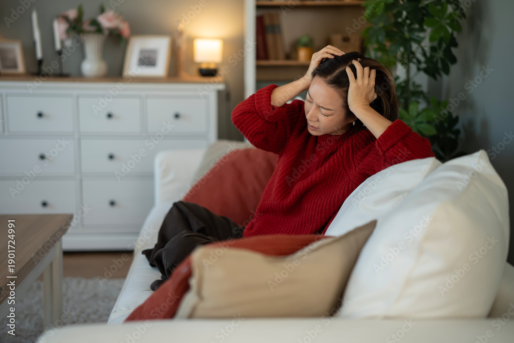 Obraz premium Stressed woman experiencing headache holding head on sofa