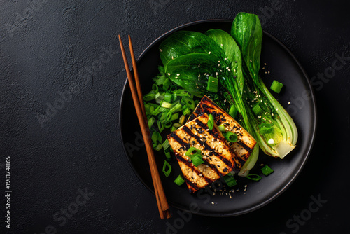 Satisfying healthy grilled tofu steak meal served with green bok choy vegetable and wooden chopstick on dark plate offering inviting wholesome nutritious vegan dinner experience