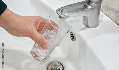 Close up of filling glass with water from sink faucet in bathroom