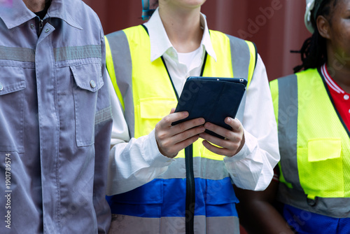 Wallpaper Mural Close up IIndustrial workers wearing reflective safety vests using a digital tablet for inspection and data review in front of cargo container Torontodigital.ca