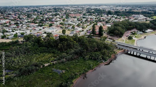 Aerial view showing homes, a river, trees, and a road with a bridge crossing the water in an urban area.