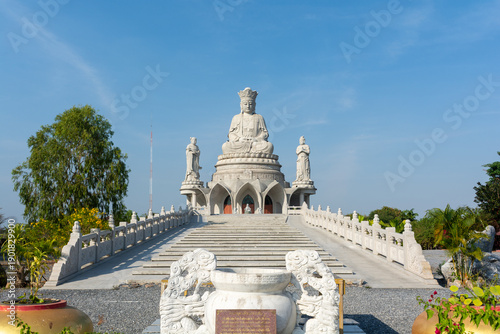 Grand white Buddha statue atop temple staircase under clear blue sky, serene spiritual landmark in Asia