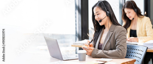 Fotografi Wide shot of professional Asian customer service team wearing headsets and working on laptops in a bright modern office