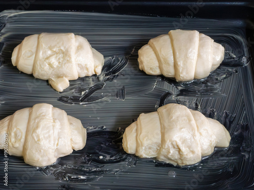 Raw Croissants with Egg Wash on a Baking Sheet.