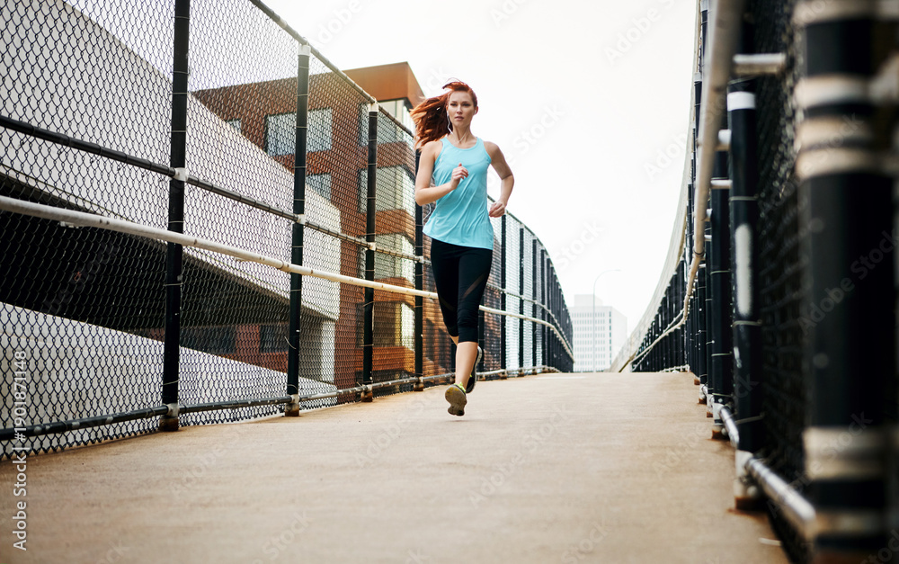 Fototapeta premium Below, running and woman in city for training, earphones and challenge for health benefits. Practice, person and runner with exercise, podcast and fitness with cardio, bridge and listening to music