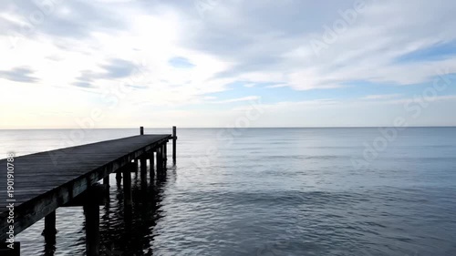 Wallpaper Mural A tranquil wooden pier extends into calm ocean water under a soft, cloudy sky. Gentle ripples reflect the peaceful light. Torontodigital.ca