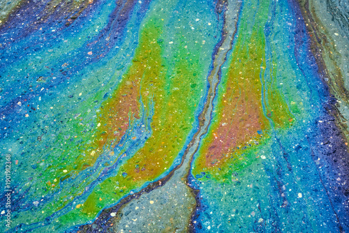 Canvas Print Oil slick creating swirling rainbow patterns on asphalt, showing iridescent colors and fluid texture