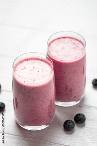 Two glasses of berry smoothie with chia and fresh berries on a white wooden table