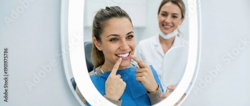 Happy woman patient checking white teeth in mirror at dental clinic, pointing to smile with satisfaction while female dentist watches Concept of oral hygiene, whitening care and stomatology health