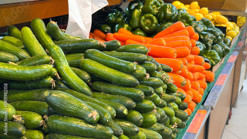 Abundant fresh cucumbers, carrots, and green bell peppers displayed in a grocery store produce aisle, ready for sale.