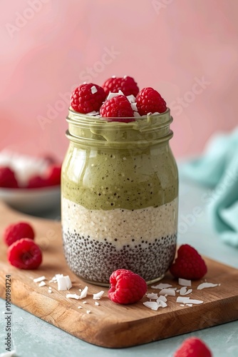 Layered chia pudding with matcha cream and raspberries in a glass jar, healthy dessert concept on wooden board, candid food art illustration with soft pink background