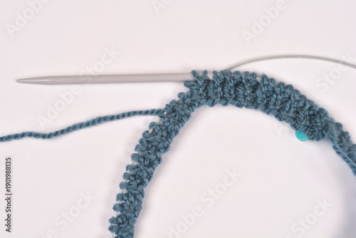 A detailed close up shot of blue textured yarn stitches on a silver circular knitting needle over a plain white background
