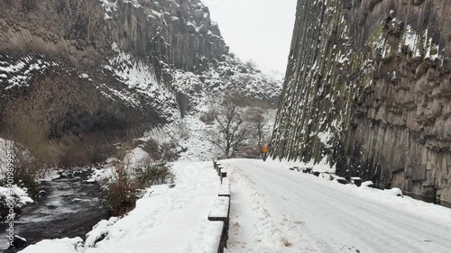 Snow-covered road runs through the Symphony of Stones canyon with towering basalt columns on both sides during winter