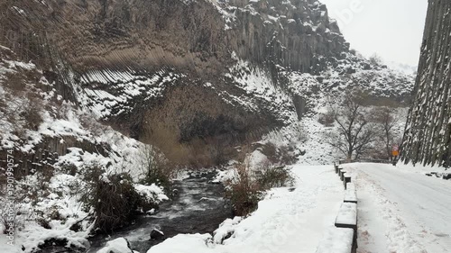 Snow-covered road runs through the Symphony of Stones canyon with towering basalt columns on both sides during winter