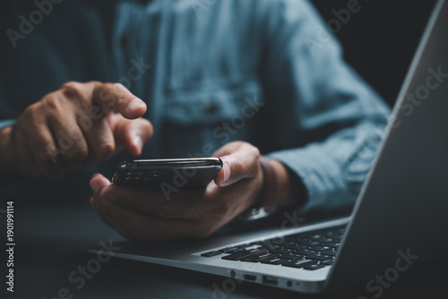 Fotografie Close-up of hands holding a black smartphone, with a laptop keyboard in the background
