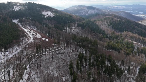 Aerial view of a winter mountain road with cars driving along a winding route as low clouds cut across snowy slopes in sunny weather.
