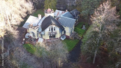 Aerial view of a grand, decaying old mansion, its yellow facade crumbling amidst bare autumn trees and green patches. A hauntingly beautiful historical gem. Obninsk, Russia
