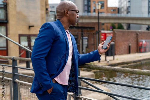 Foto Man in blue suit looks at smartphone near water in urban area during daytime