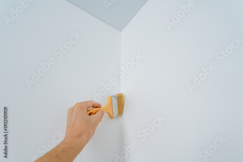 Hand Painting Interior Wall Corner With Small Brush For Precise Trim Finishing, Careful Strokes Along Seam Create Smooth White Finish, Intimate Diy Touchup During Home Renovation