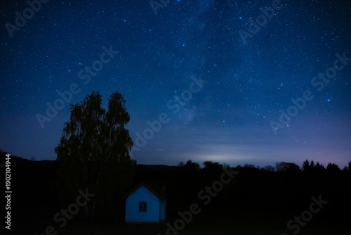 Milky Way stars with countryside tree and landscape silhouettes.