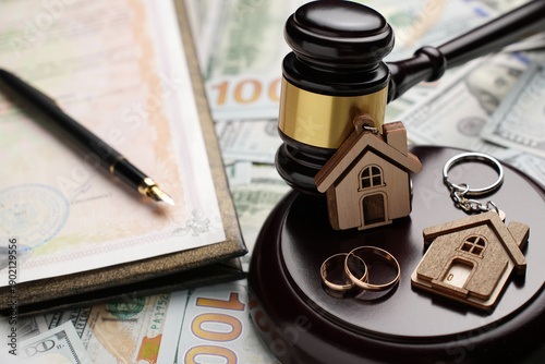 Property Division in Divorce and Marital Law Concept. Gold wedding rings, wooden house model, and a judge gavel on legal paperwork and US currency. Division, alimony, and real estate legal disputes