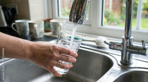 Person fills glass with water from kitchen faucet in home during daytime