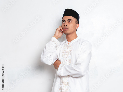 Konstfotografi portrait of a young Indonesian Muslim man wearing a white traditional koko shirt and a black peci cap, performing the adzan (Islamic call to prayer)