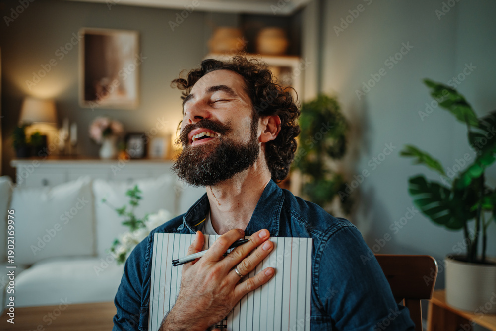 Obraz premium Bearded man expressing gratitude holding notebook at home