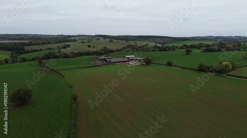 Aerial drone footage pushing in over a rural cow farm in Derbyshire, England, showing farmland and fields. Suitable for agriculture, rural business, sustainability, and countryside establishing shots.