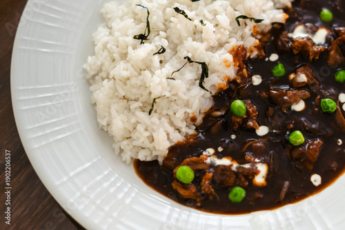 Japanese beef stew with rice and green peas served on white plate, hearty asian meal with rich brown sauce.