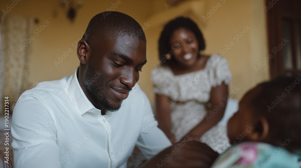 Obraz premium African man in white shirt caring for baby at home, warm family bonding and gentle parenting mood, young African mother smiling in soft focus
