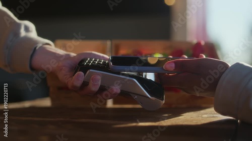 Closeup of unrecognizable buyer handing smartphone to farm vendor during fresh strawberry purchase at rustic outdoor market stall
