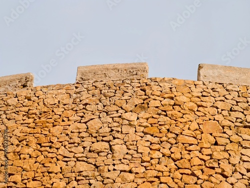 Quadro su tela Sunshine illuminates aged stone battlements atop historic fortress against expan